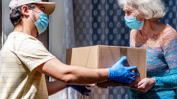Man wearing PPE delivering a package to a senior woman